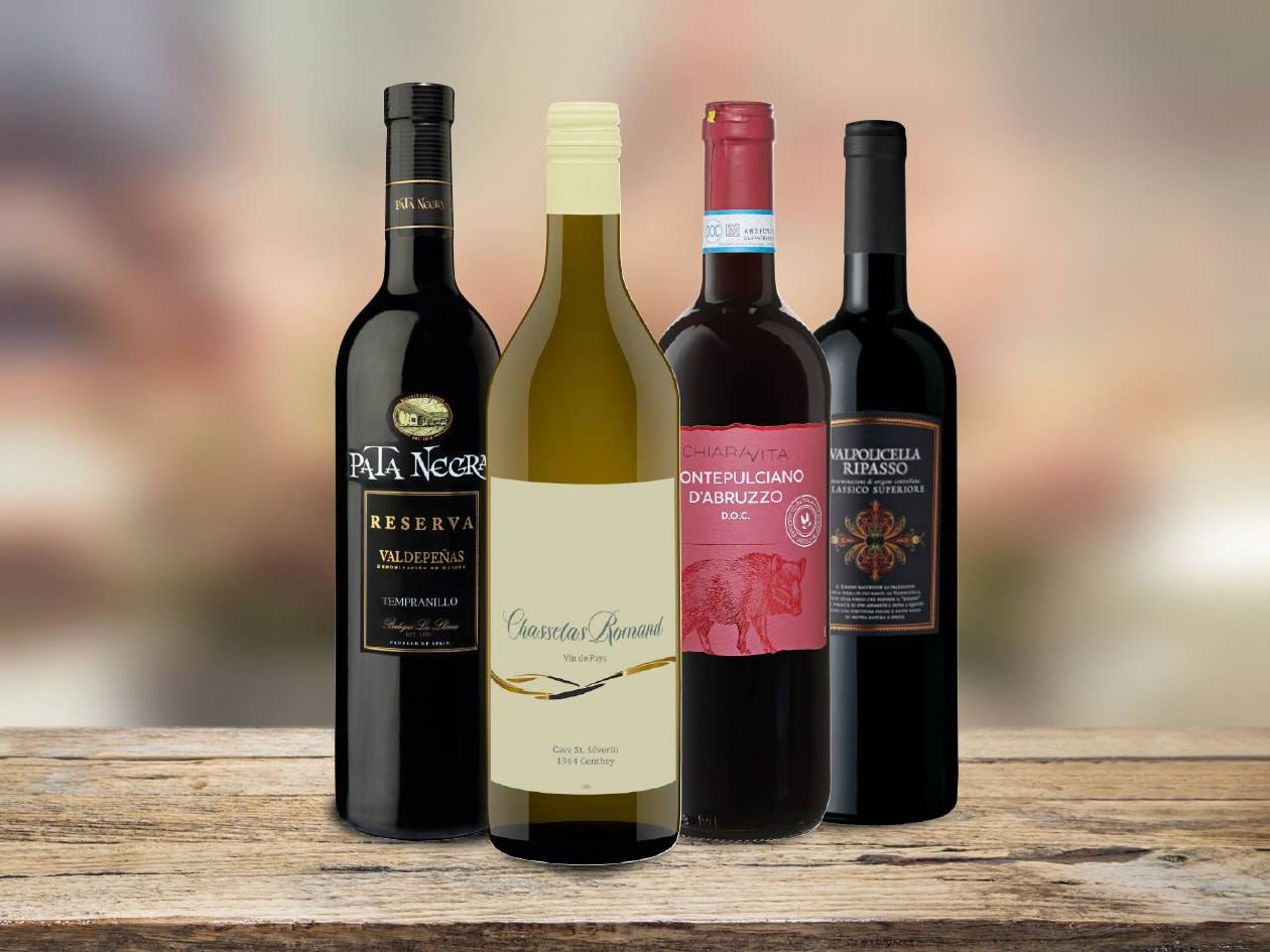 Quatre bouteilles de vin, dont Pata Negra Reserva et Valpolicella Ripasso, sur une table en bois.