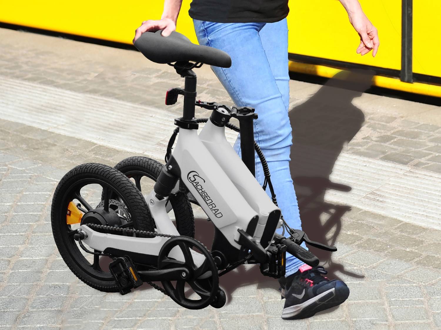 Bicicletta elettrica pieghevole bianca tenuta da una persona in jeans su un marciapiede.