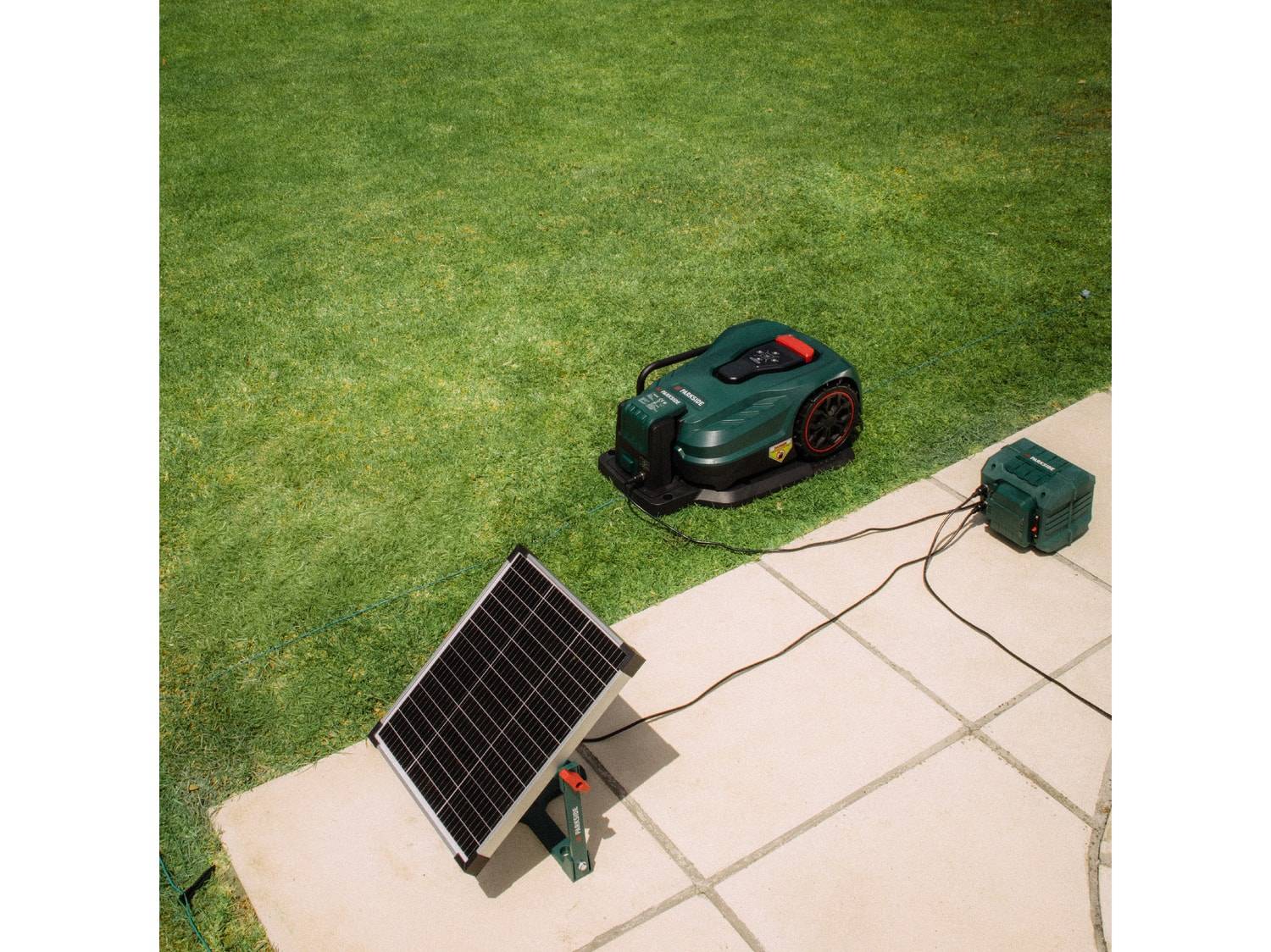 Grüner Mähroboter mit Ladestation und Solarpanel auf Rasen und Terrasse.
