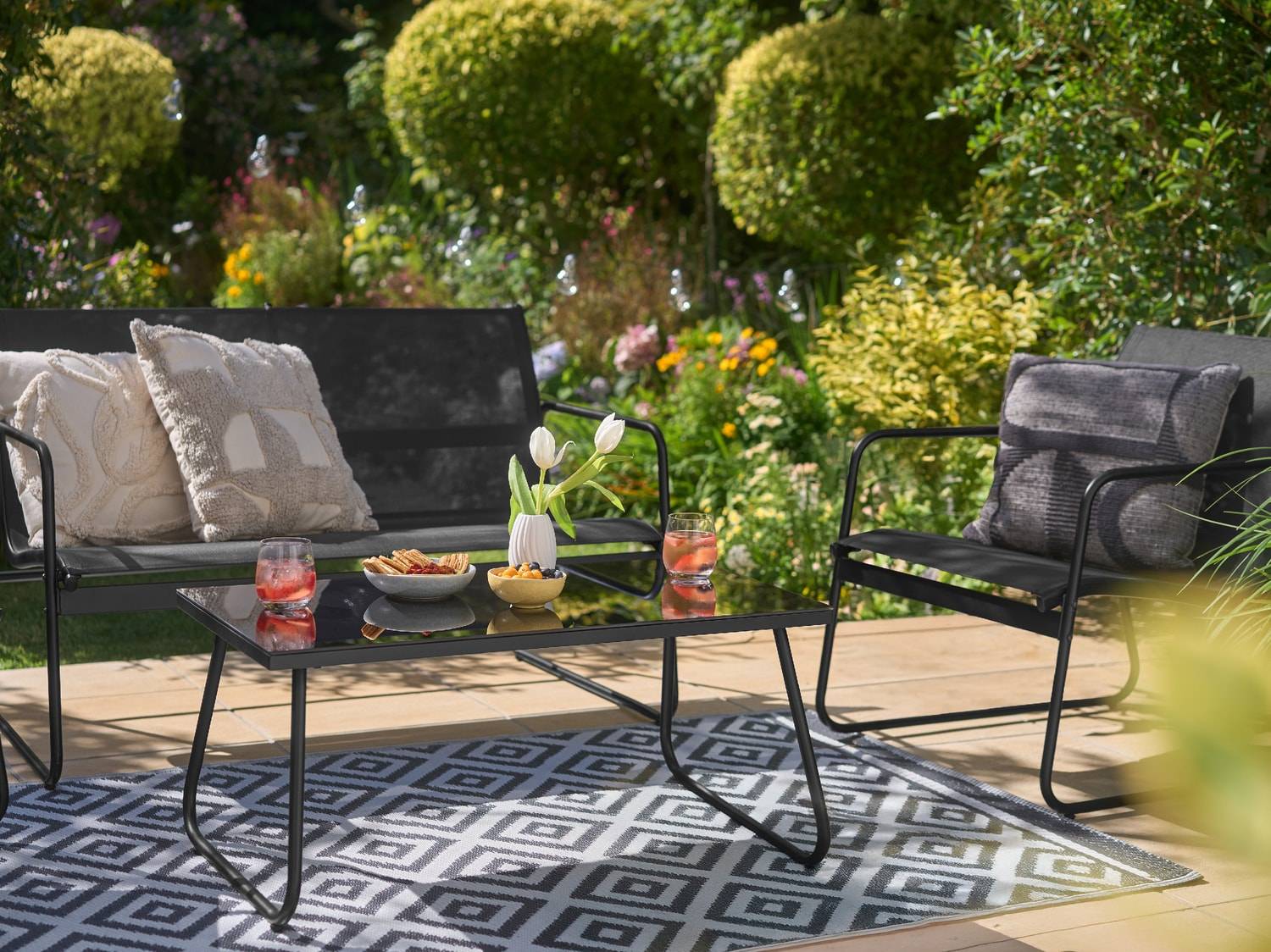 Schwarze Gartenlounge mit Couchtisch, Sofa und Sessel auf einem geometrischen Teppich.
