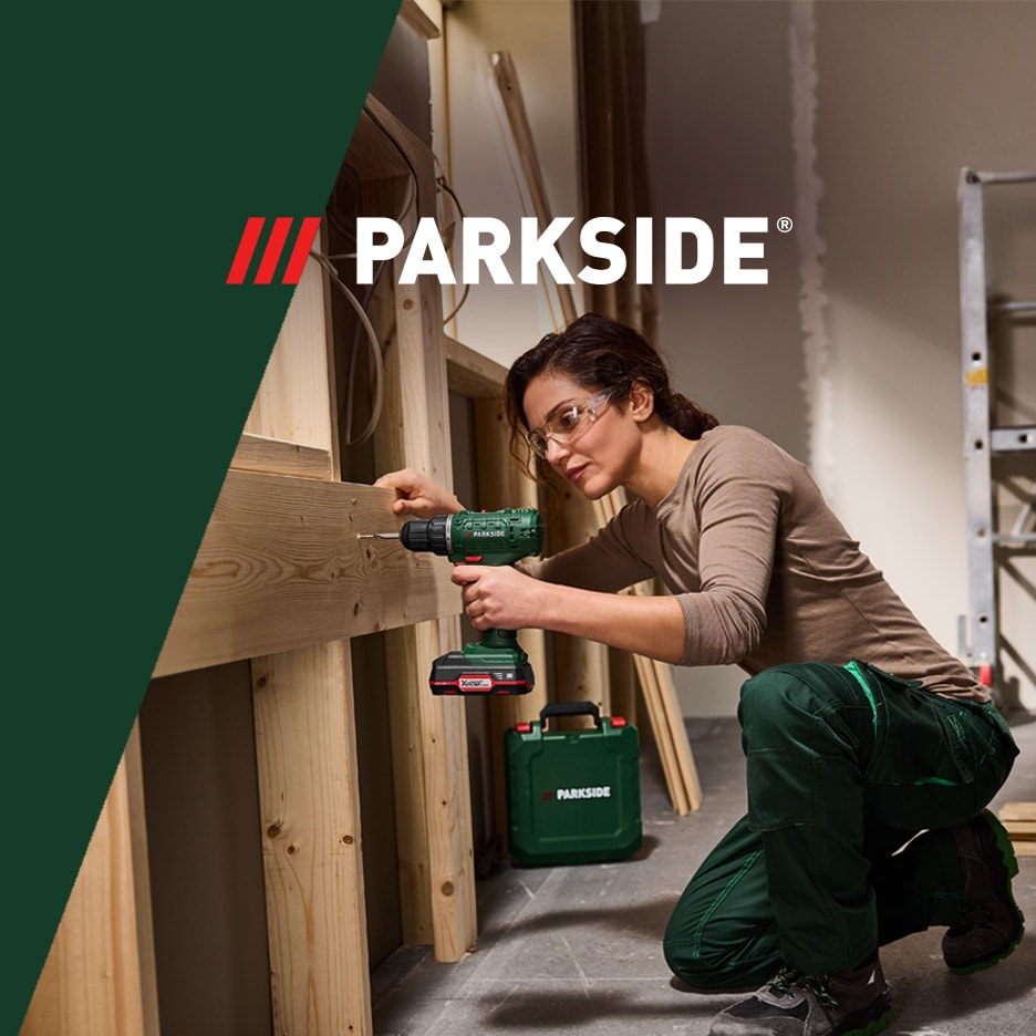 Frau mit Akku-Bohrschrauber und Schutzbrille, die an einer Holzkonstruktion arbeitet.