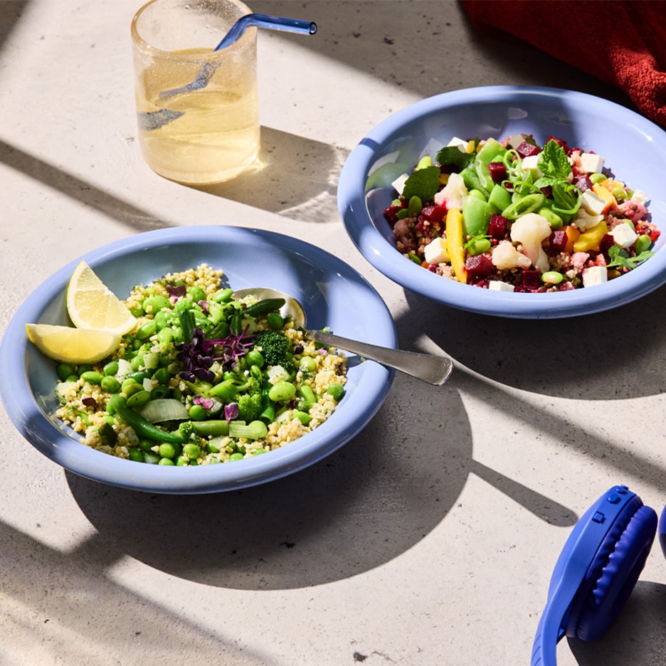 Zwei Schalen bunter Salat mit Gemüse, Getreide und Zitrone, dazu ein Getränk und Kopfhörer.