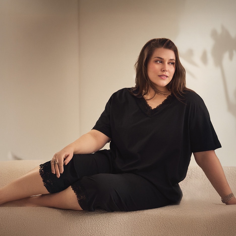 Frau in schwarzem Pyjama mit Spitze sitzt auf einem Sofa