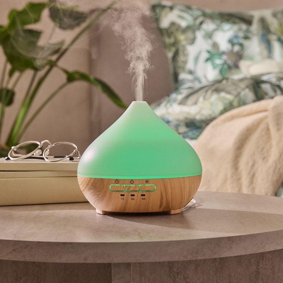 Grüner und hölzerner Aromadiffusor mit Dampf, Brille und Pflanze in einem Schlafzimmer.