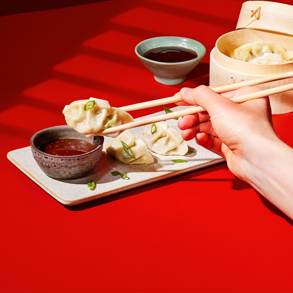 Gyoza mit Sauce und Essstäbchen auf rotem Hintergrund.