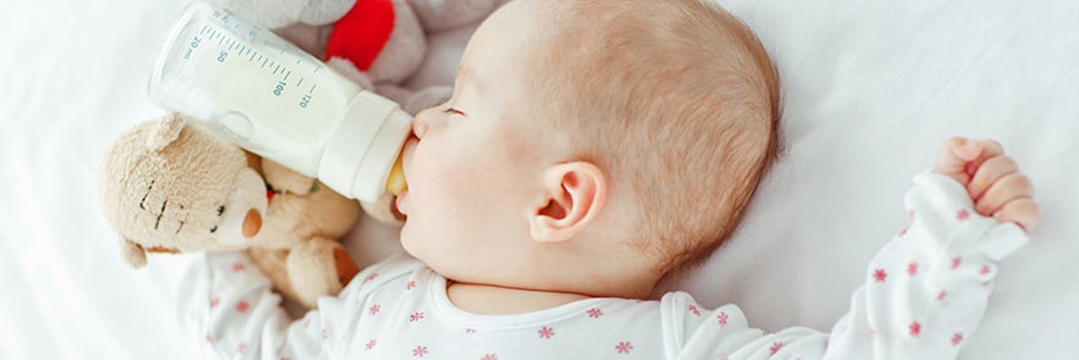 Neonato che dorme con biberon e orsacchiotto.