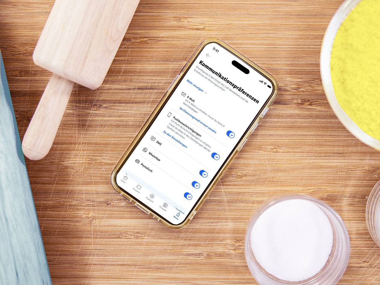Smartphone mit Kommunikationspräferenzen auf einem Holztisch mit Backutensilien.