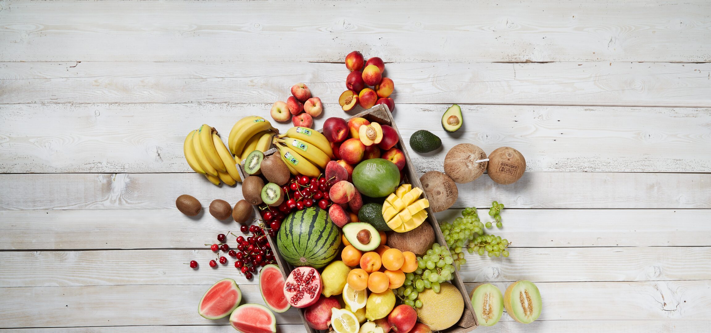 Una cassa di legno piena di frutta fresca biologica, tra cui banane, meloni, mele e avocado.