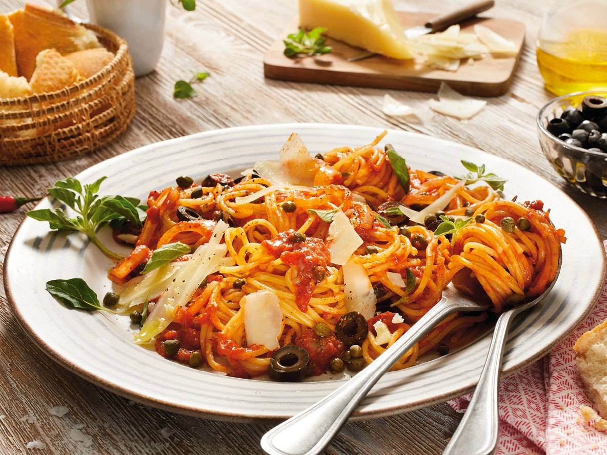 Spaghetti Puttanesca mit Kapern, Oliven, Tomaten und Käsesplittern.