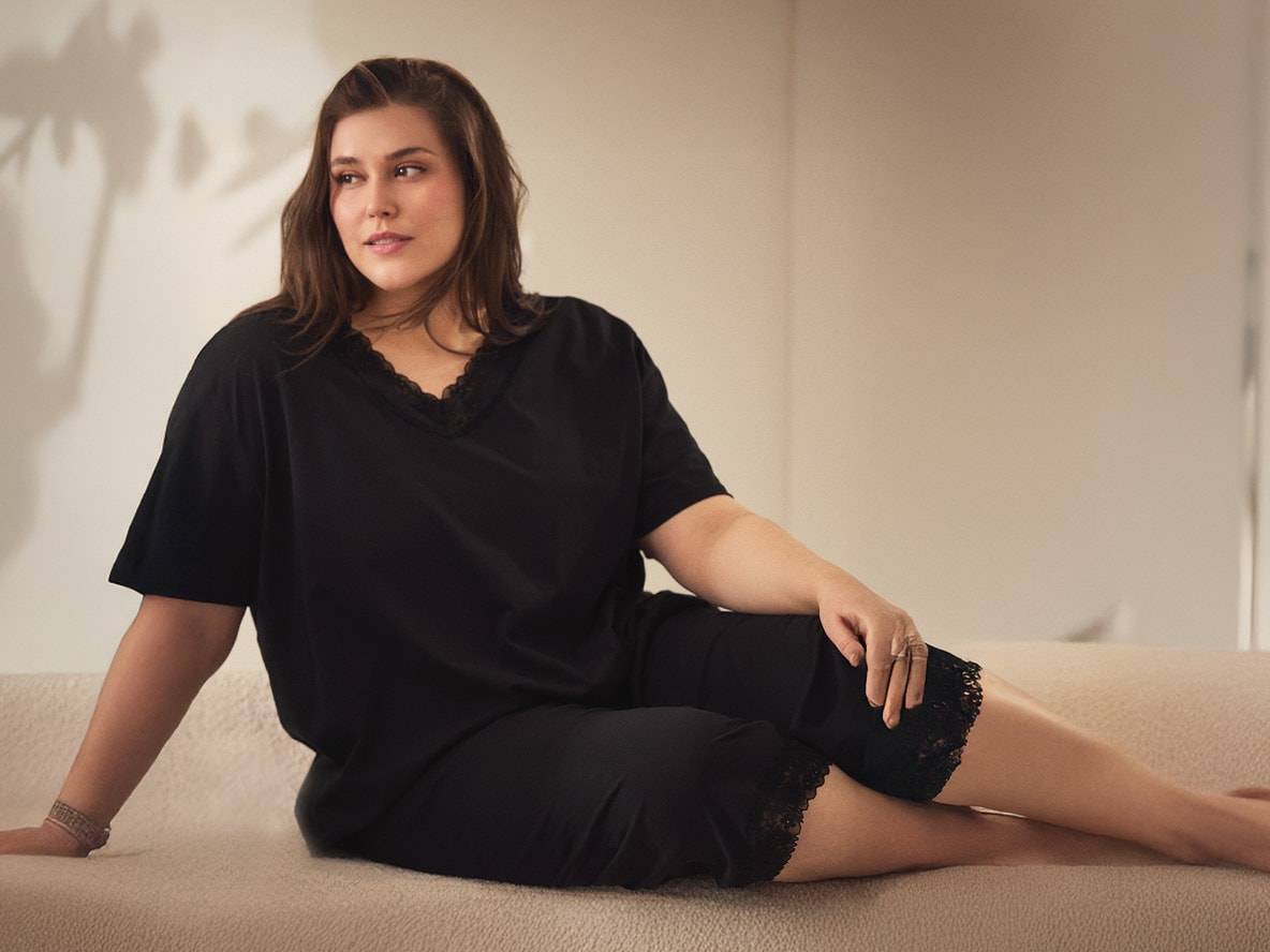 Frau in schwarzem Pyjama mit Spitze, auf einem hellen Sofa sitzend.