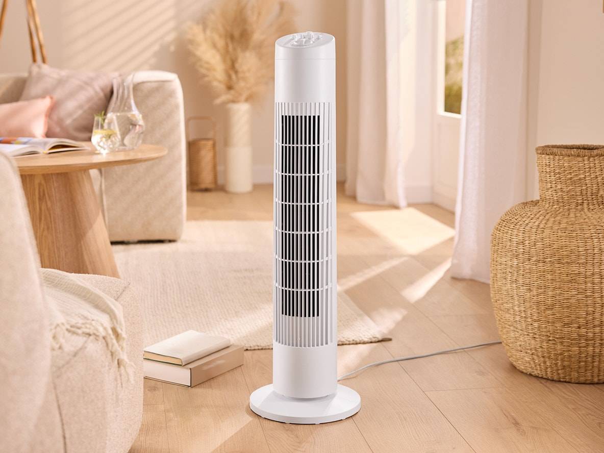 Weißer Turmventilator in einem hellen Wohnzimmer mit Sofa und Couchtisch.