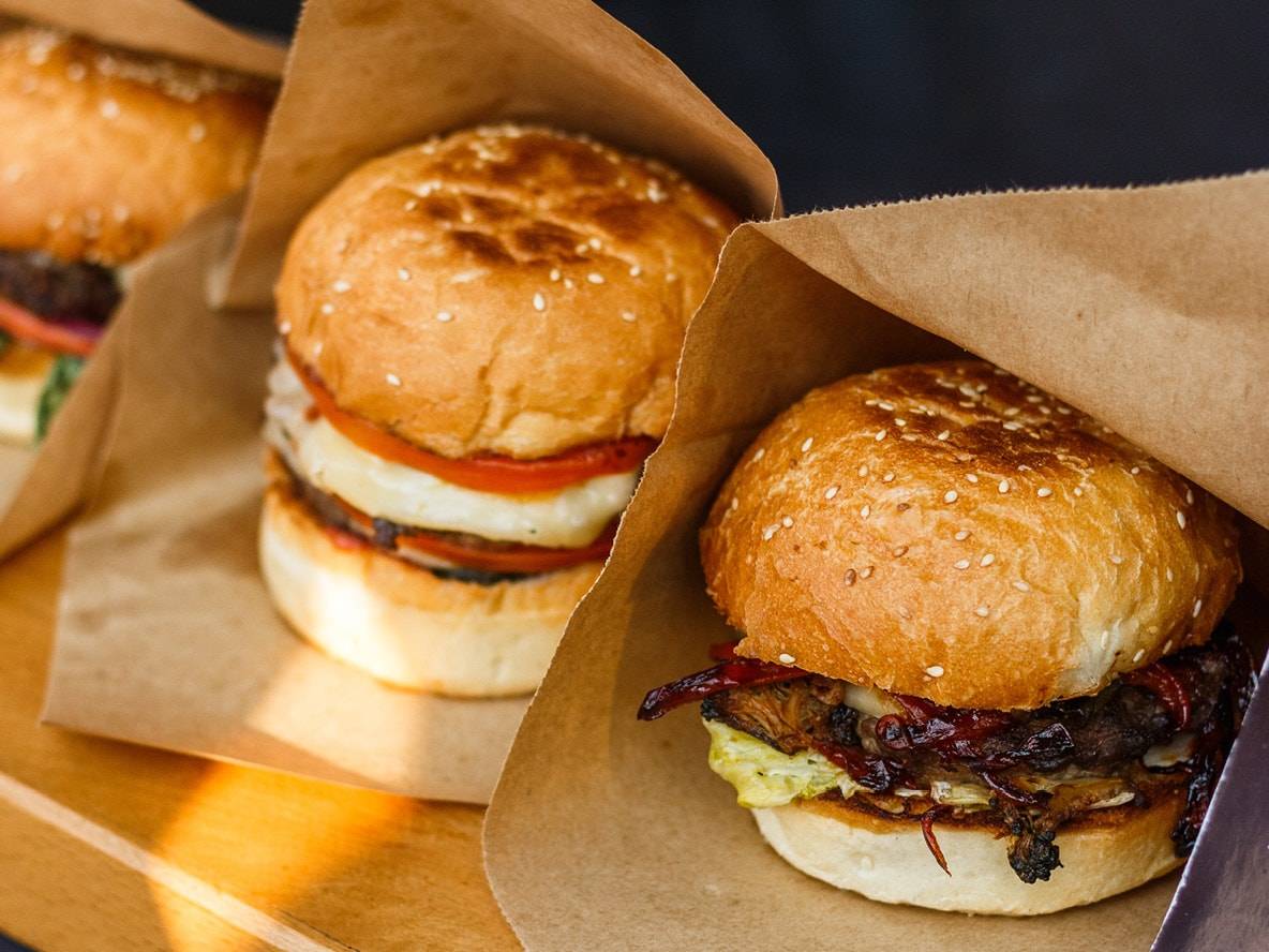Drei Burger in Papiertüten, mit verschiedenen Belägen.