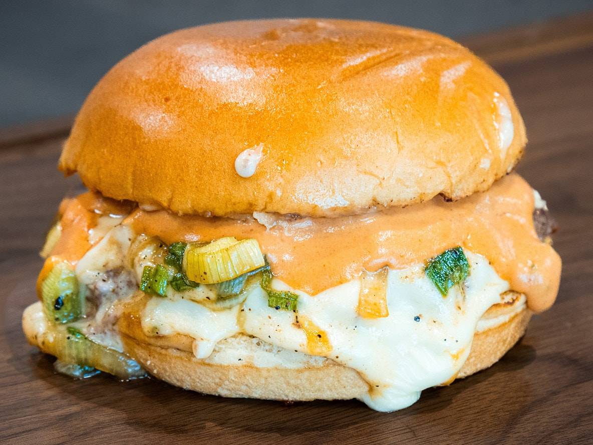 Burger mit geschmolzenem Käse, cremiger Soße und Frühlingszwiebeln auf Holzbrett.