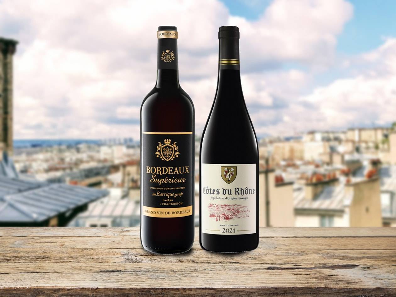Zwei Flaschen Rotwein, Bordeaux Supérieur und Côtes du Rhône, auf einem Holztisch mit Blick auf Paris.