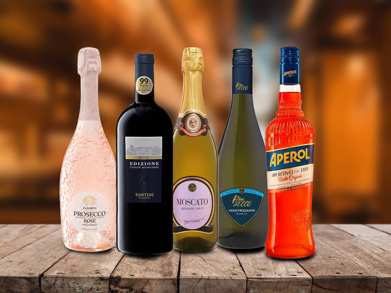 Fünf Flaschen Wein und Aperitif, darunter ein Rosé-Prosecco, ein Rotwein und ein oranger Aperitif, auf einem Holztisch.