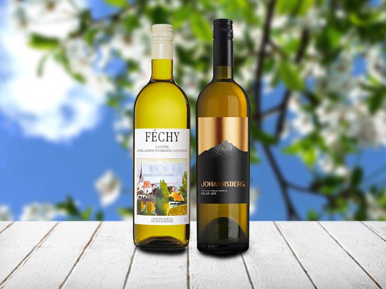 Zwei Flaschen Weißwein auf einem Holztisch vor einem blauen Himmel mit blühenden Bäumen.