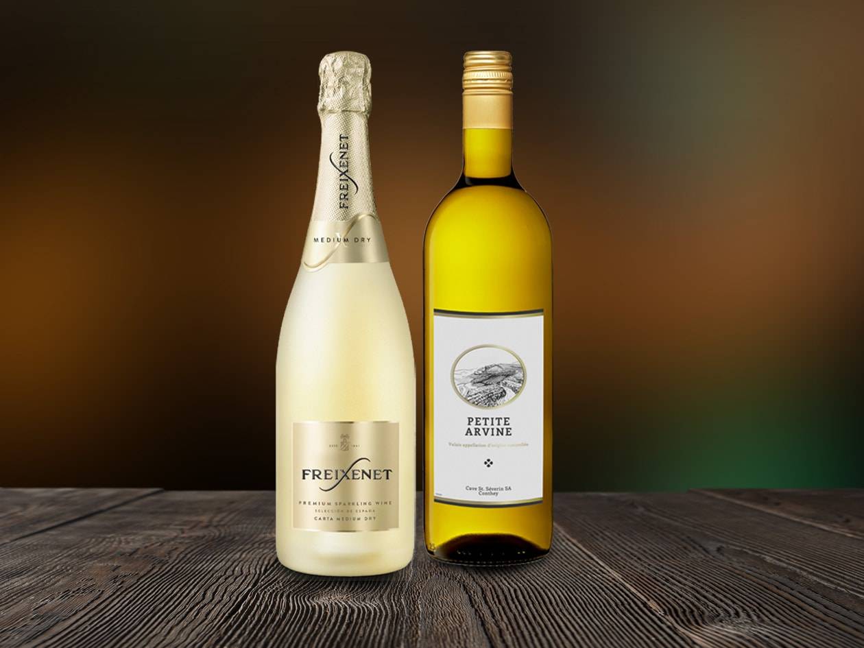 Zwei Weinflaschen, ein Sekt und ein Weißwein, auf einem Holztisch.